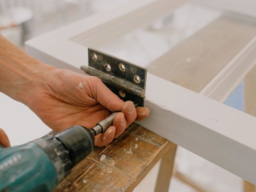 Technician fastening a metal hinge with a cordless drill
