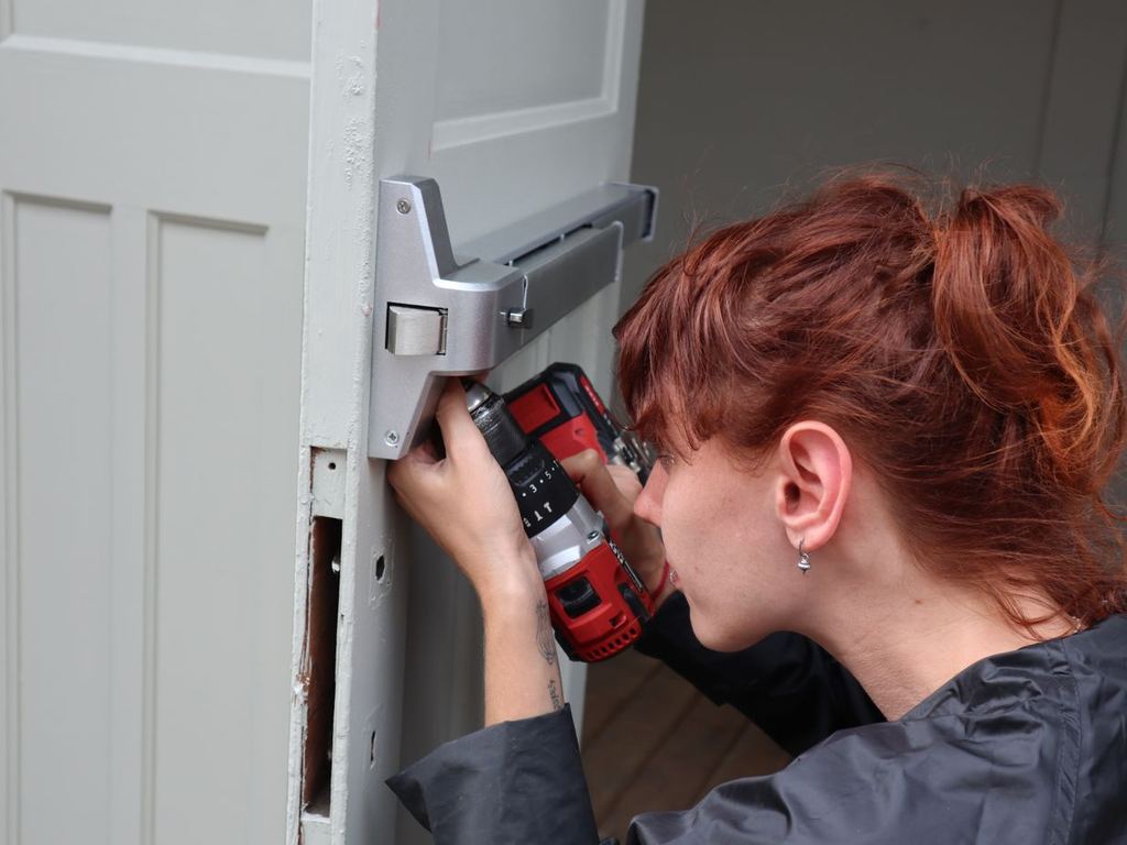 Technician repairing a commercial door latch with a power drill