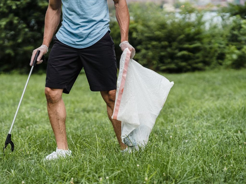 Worker using a grabber to collect litter into a bag