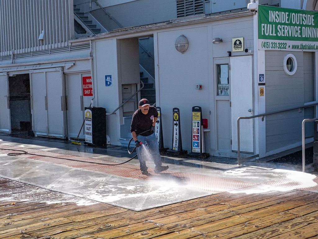 Worker pressure washing a sidewalk outside a commercial building