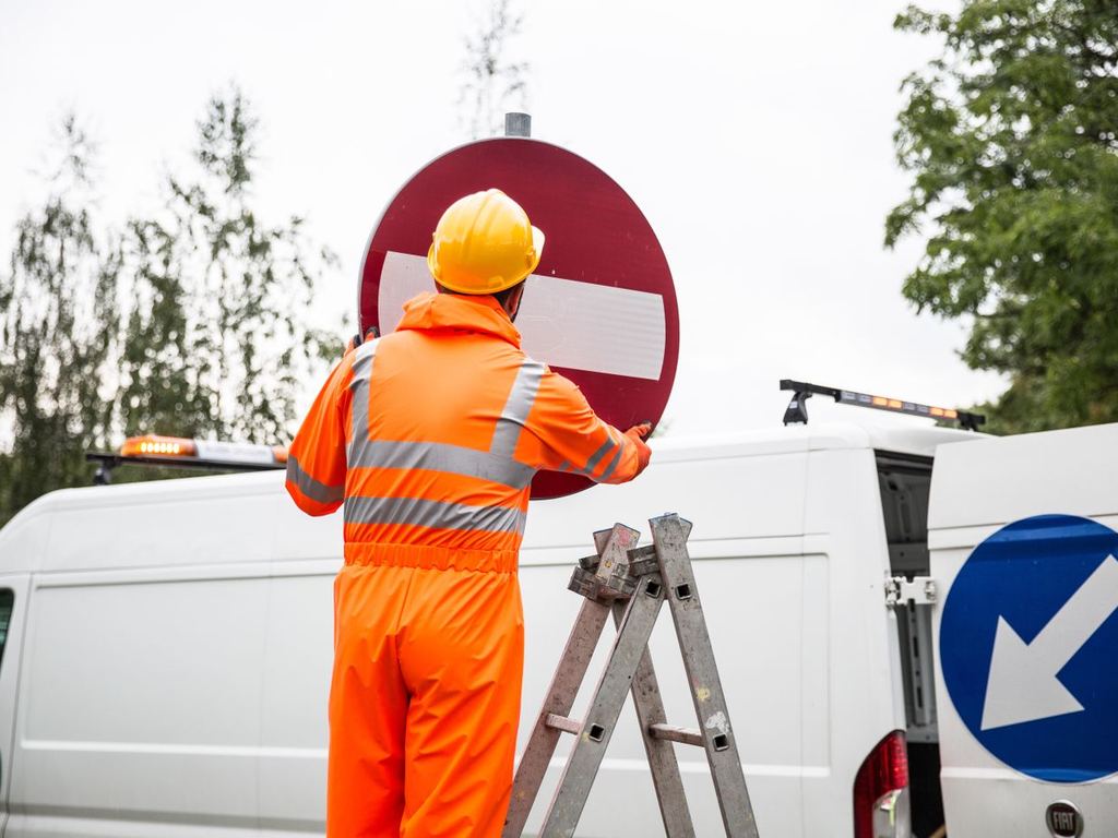 Worker installing a sign from a ladder beside a service van